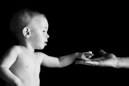 Baby is holding father's hand. Over black background.の写真素材