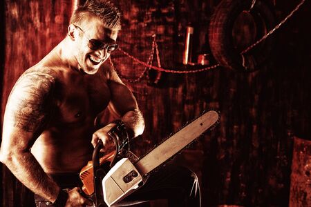 Handsome muscular man with a chainsaw in the old garage.の写真素材