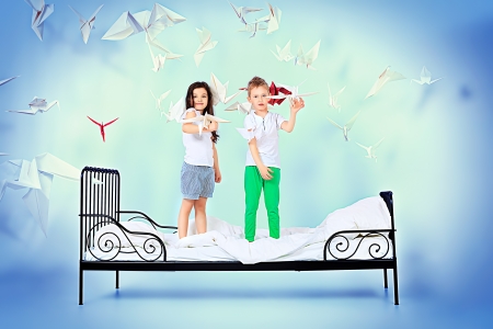 Cute kids standing together on the bed under the blanket. Dream world.の写真素材