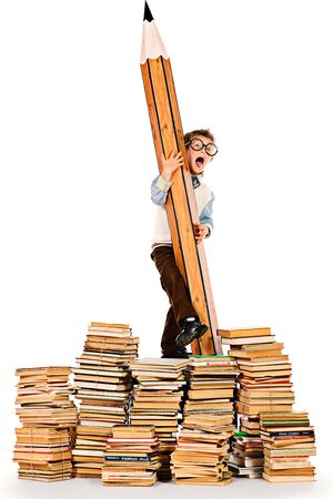 A boy standing on a pile of books and holding a huge pencil. Education. Isolated over white.の写真素材