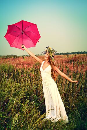 Romantic smiling young woman in light summer dress standing in the meadow with umbrella.の写真素材
