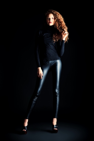 Charming fashion model with beautiful curly hair posing at studio. Over black background.の写真素材