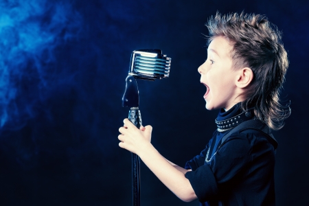 Emotional little boy is singing into a microphone like a rock musician. の写真素材