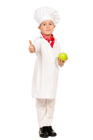 Full length portrait of a little boy cook holding green apple. Different occupations. Isolated over white background.の写真素材