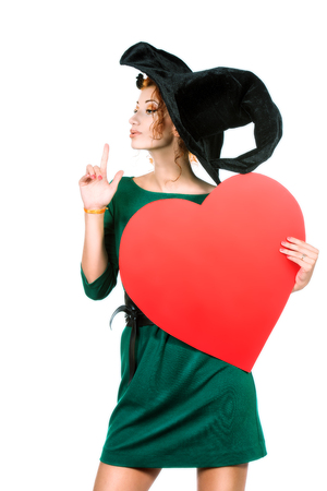 Charming red-haired witch holding red heart. Halloween. Isolated over white. の写真素材