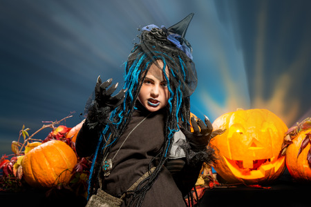 Little girl in a costume of witch posing with pumpkins over dark background.の写真素材