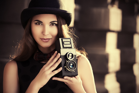 Beautiful brunette standing on a city street and holding the old camera. Retro style.の写真素材