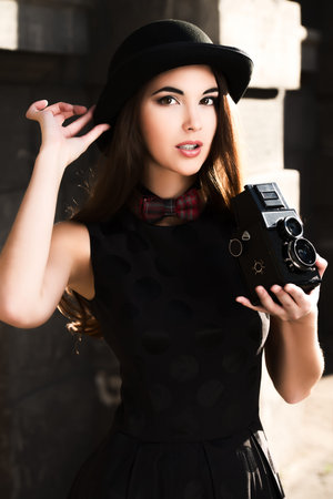 Beautiful brunette standing on a city street and holding the old camera. Retro style.