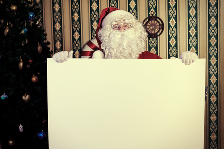 Santa Claus holding white board over home background. の写真素材