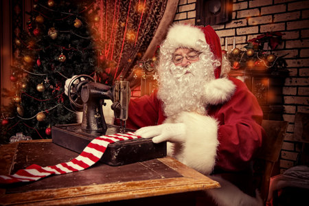 Santa Claus is sewing on a sewing machine striped socks for Christmas.の写真素材