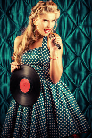 Pretty pin-up woman singing with vinyl record over vintage background.の写真素材