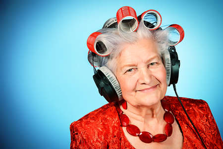 Elderly woman in curlers listening to music in headphonesの写真素材