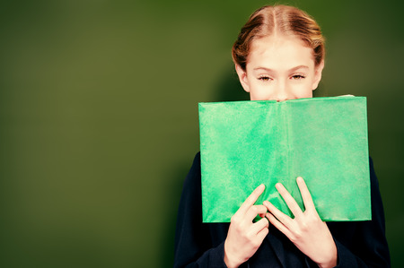 Smiling schoolgirl standing near the blackboard with a book. Education.の写真素材