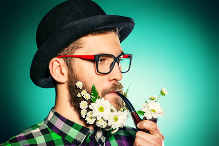 Handsome smiling young man in glasses and a beard of flowers. 