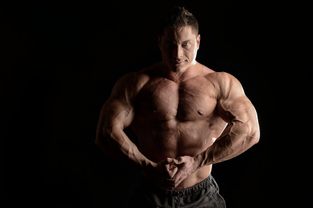 Handsome muscular bodybuilder posing over black background.の写真素材
