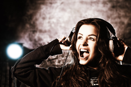 Beautiful expressive girl listening to music in headphones and singing. Grunge style. Disco, party.の写真素材