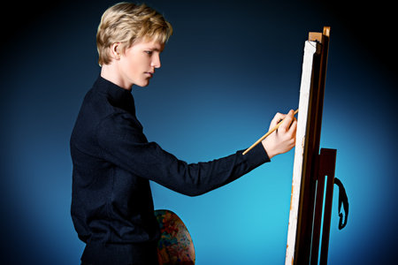 Young man artist paints on canvas with oil paints. Studio shot over black background.の写真素材