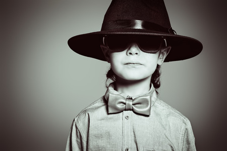 Portrait of a cute 7 year old boy wearing elegant hat and bow-tie with sunglasses. の写真素材