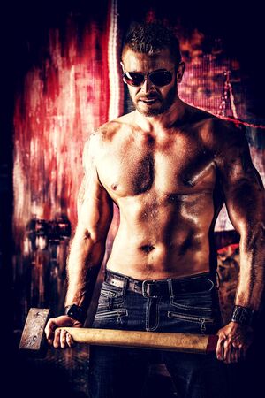 Handsome muscular man with sledgehammer working in the old garage.の写真素材