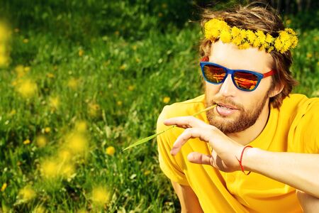 Handsome young man sitting on a grass and smiles dreamily. Summer rest, vacation.の写真素材