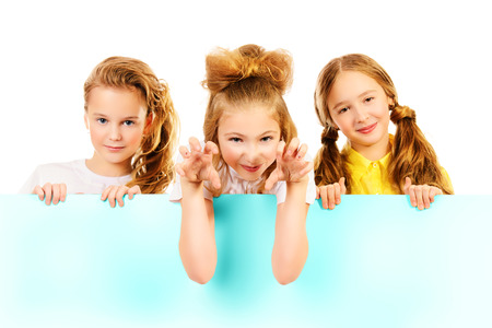 Three smiling girls standing together and hold white board. Isolated over white.の写真素材