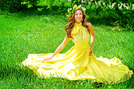 Romantic young woman in beautiful yellow dress sitting on a green lawn in the garden. の写真素材