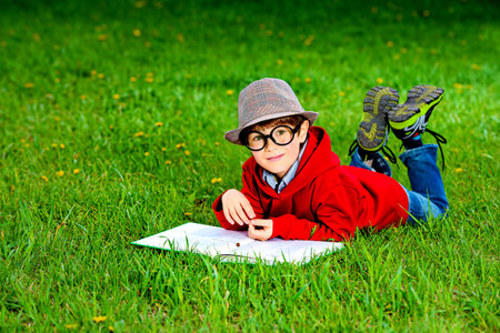 Cute 7 years old boy lying on a grass and reading a book. Summer day. 