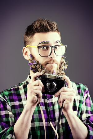 Extravagant young man with a beard of flowers making photographs. の写真素材