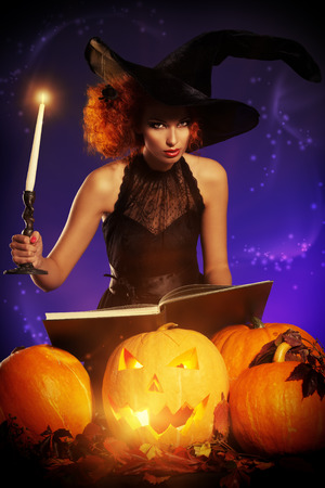 Beautiful red-haired witch casts a spell over pumpkins. Halloween.の写真素材