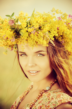 Romantic girl in a wreath of wild flowers standing in a field. Summer life.の写真素材