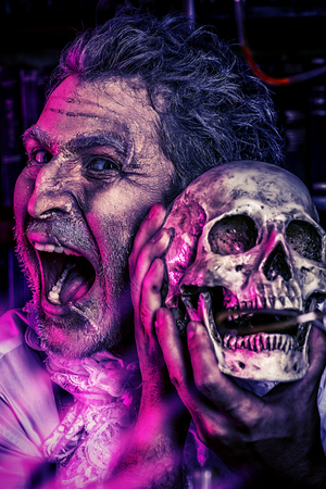 Close-up portrait of an old medieval scientist holding a skull. Alchemist. Halloween.の写真素材