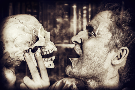 Close-up portrait of an old medieval scientist holding a skull. Alchemist. Halloween.の写真素材