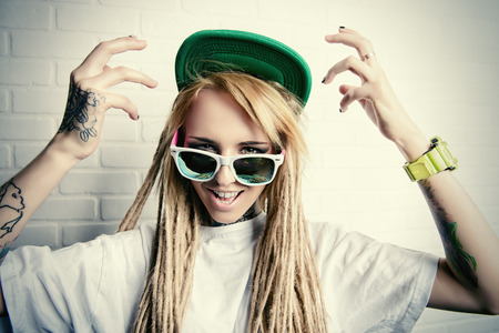 Modern teenage girl with blonde dreadlocks standing by the brick wall. Jeans style. Modern generation.の写真素材