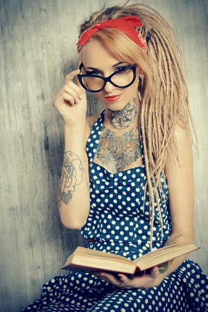 Close-up portrait of a modern pin-up girl wearing old-fashioned polka-dot dress and spectacles and modern dreadlocks. Fashion shot. Tattoo.の写真素材