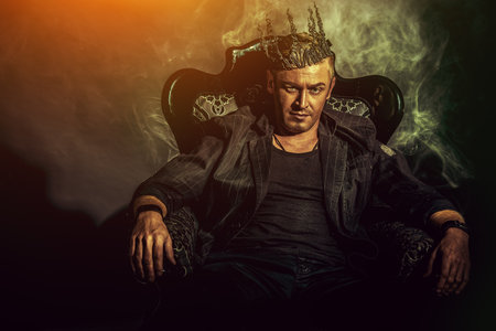 Portrait of a masculine handsome man in elegant black suit sitting in a chair in a classic vintage style.の写真素材