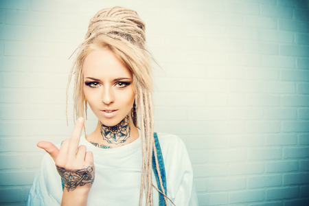 Modern teenage girl with blonde dreadlocks standing by the brick wall. Jeans style. Modern generation.の写真素材