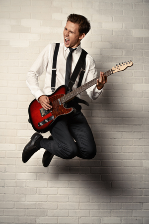 Expressive young man playing rock-n-roll music on his electric guitar. Retro, vintage style.の写真素材