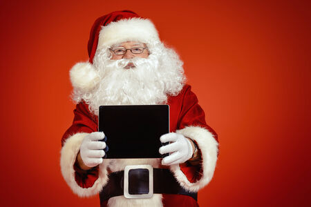 Modern Santa Claus using tablet pc over red background. Christmas.の写真素材