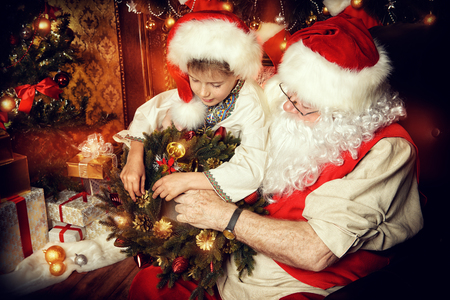 Santa Claus in his everyday clothes in Christmas home décor. Happy little boy helps Santa Claus get ready for Christmas.の写真素材