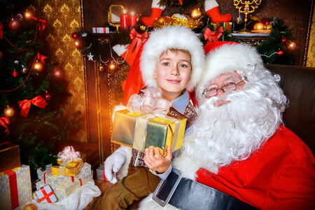 Happy little boy sitting on the lap of Santa Claus and rejoice a gift. Christmas decoration.の写真素材