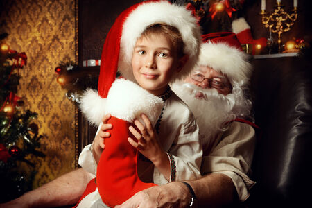 Santa Claus in his everyday clothes in Christmas home décor. Happy little boy helps Santa Claus get ready for Christmas.の写真素材
