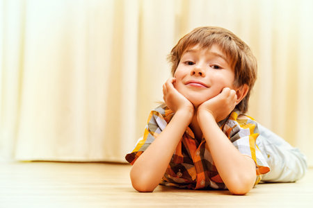 Happy smiling boy lying on a floor at home. Happy childhood.の写真素材