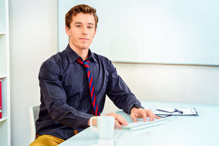 Handsome businessman working at the office on his laptop and friendly smiling at camera.の写真素材
