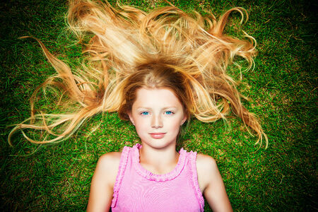 Beautiful smiling girl lying on a green lawn in the park. Sunny summer day.の写真素材