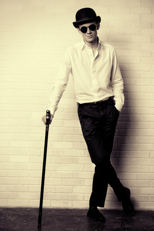 Fashion shot of a modern young man in white shirt, black bowler hat and round sunglasses.の写真素材