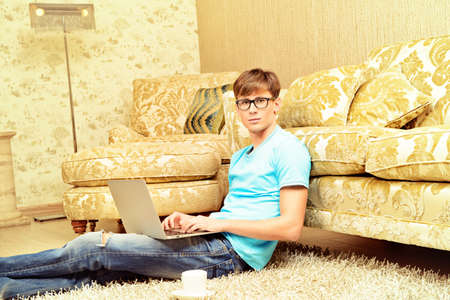Casual young man sitting on the floor with a laptop in the comfort of his home.の写真素材