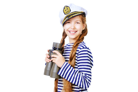 Joyful teen girl wearing sailor's striped vest and marine cap standing with binoculars. Studio shot. Isolated over white.の写真素材