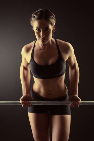 Strong young woman with beautiful athletic body doing exercises with barbell. Fitness, bodybuilding. Health care.の写真素材