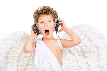 Happy little boy in a costume of angel listening to music in headphones