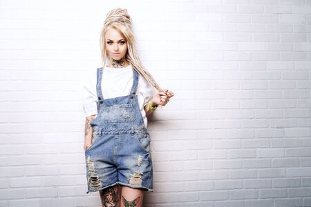 Modern teenage girl with blonde dreadlocks standing by the brick wall. Jeans style. Modern generation.の写真素材